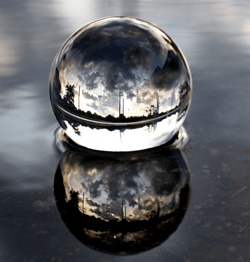 A reflective glass sphere on a wet surface with cloudy sky reflections.