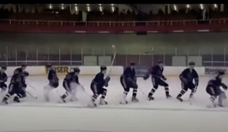 Hockey players lined up skating on ice rink.