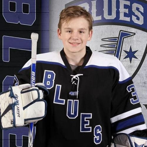Young hockey player in Blues jersey holding a hockey stick.