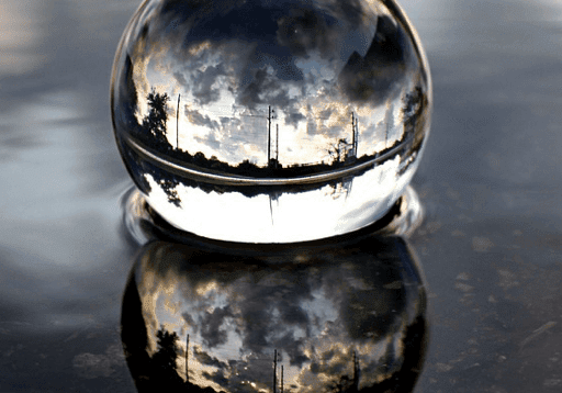 A reflective glass sphere on a wet surface with cloudy sky reflections.