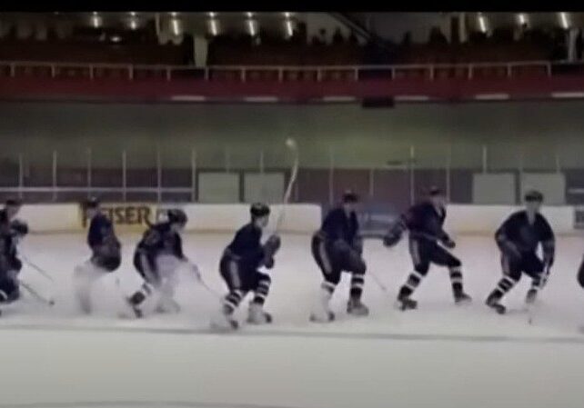 Hockey players lined up skating on ice rink.