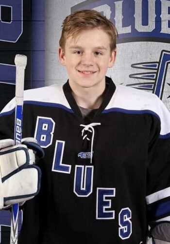 Young hockey player in Blues jersey holding a hockey stick.